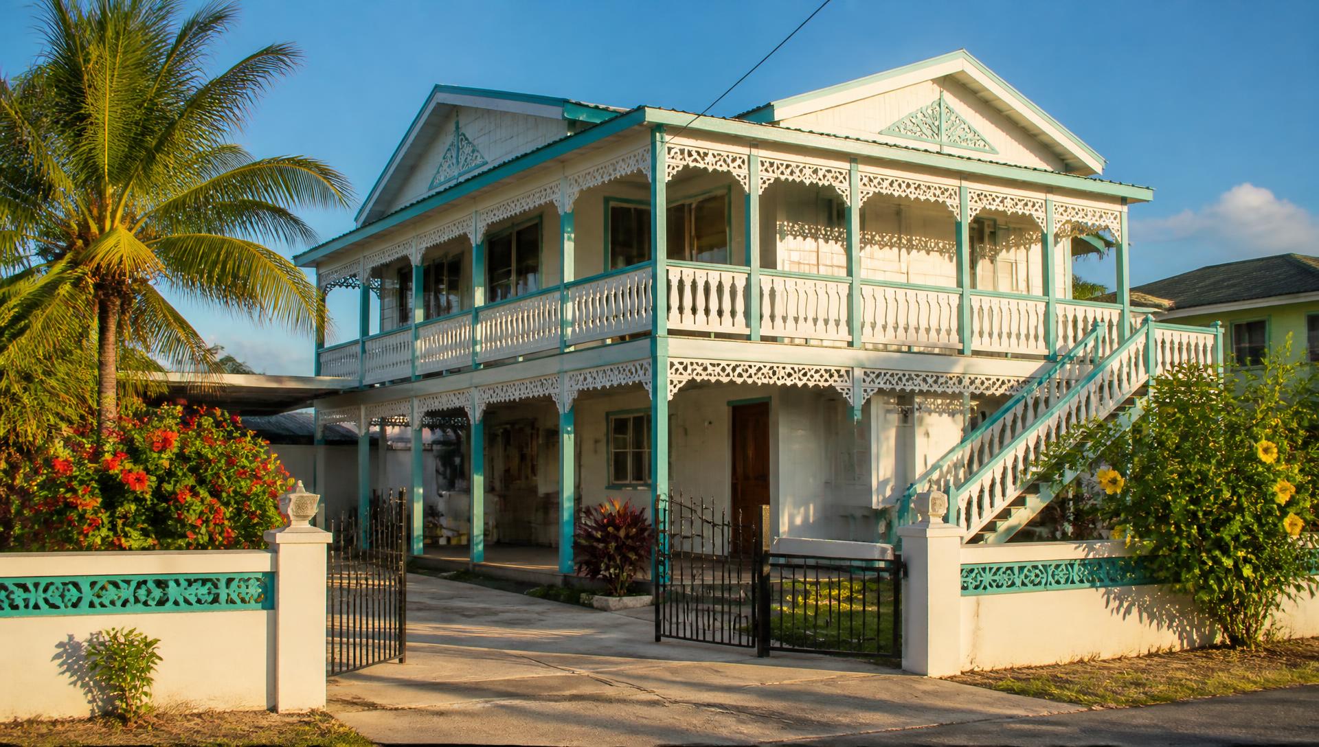 Bright two-storey Guyanese family home with fretwork verandah and palms in the front yard